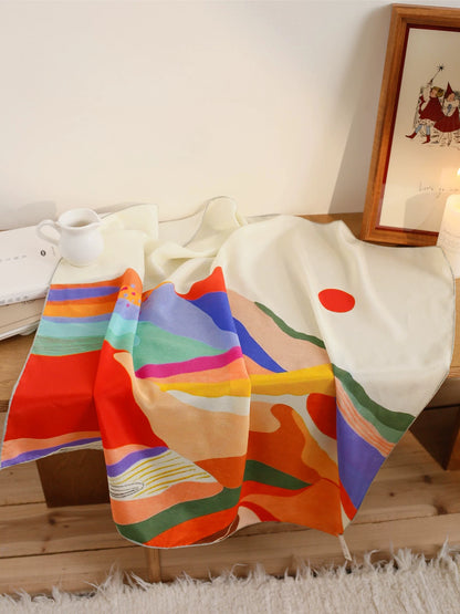 Hand-painted abstract sunset mountain mulberry silk scarf displayed on a bed, showing colorful waves and red sun artwork