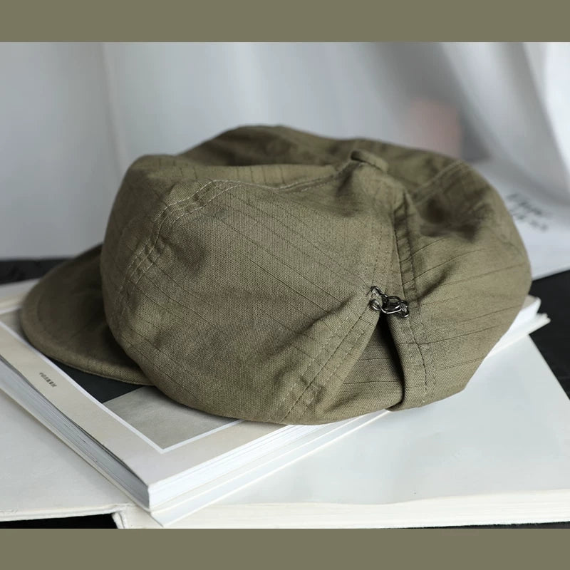 Bean green slouchy cotton beret hat with elastic adjustable fit, shown on a book for casual everyday styling