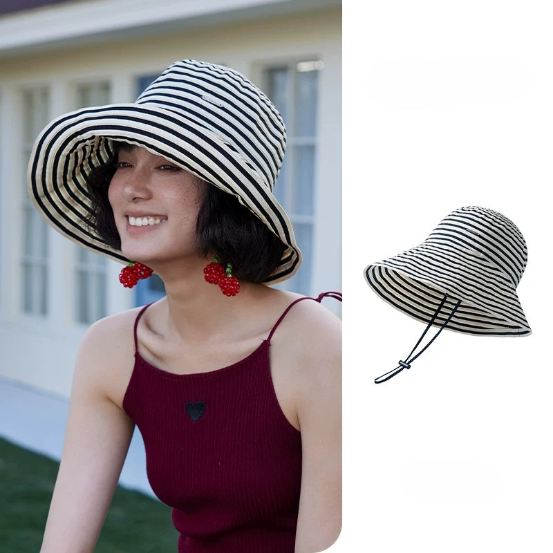 Woman wearing a beige and black striped foldable wide brim sun hat with adjustable chin strap.