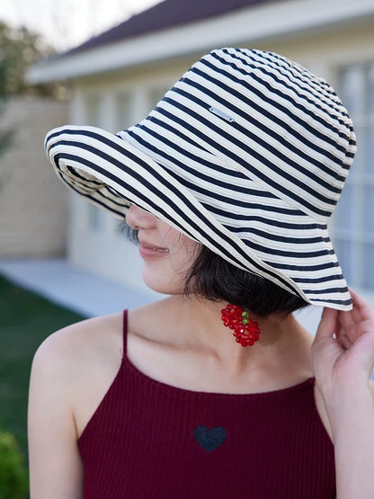 Woman adjusting a packable striped sun hat with a soft curved brim for outdoor summer wear.
