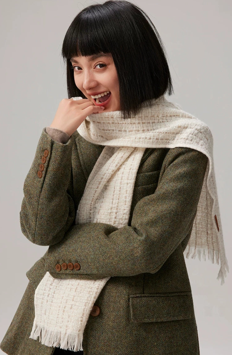 Beige cashmere tweed scarf worn over an olive blazer, with one fringed end draped behind the shoulder.