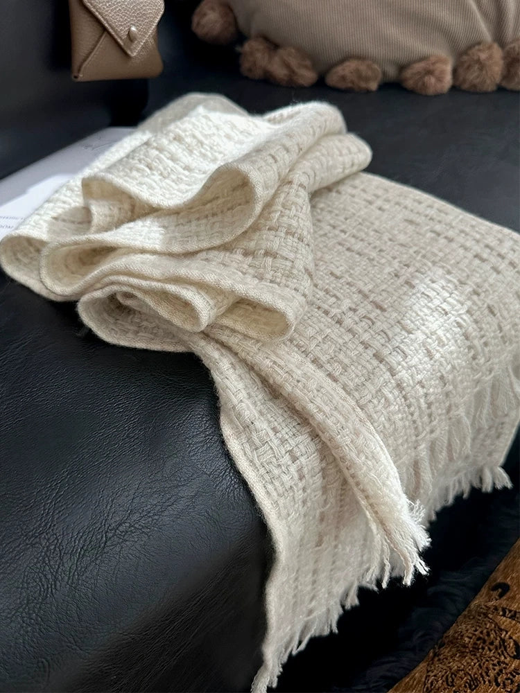 Folded beige cashmere tweed scarf on a dark chair, showing its woven texture and fringe.