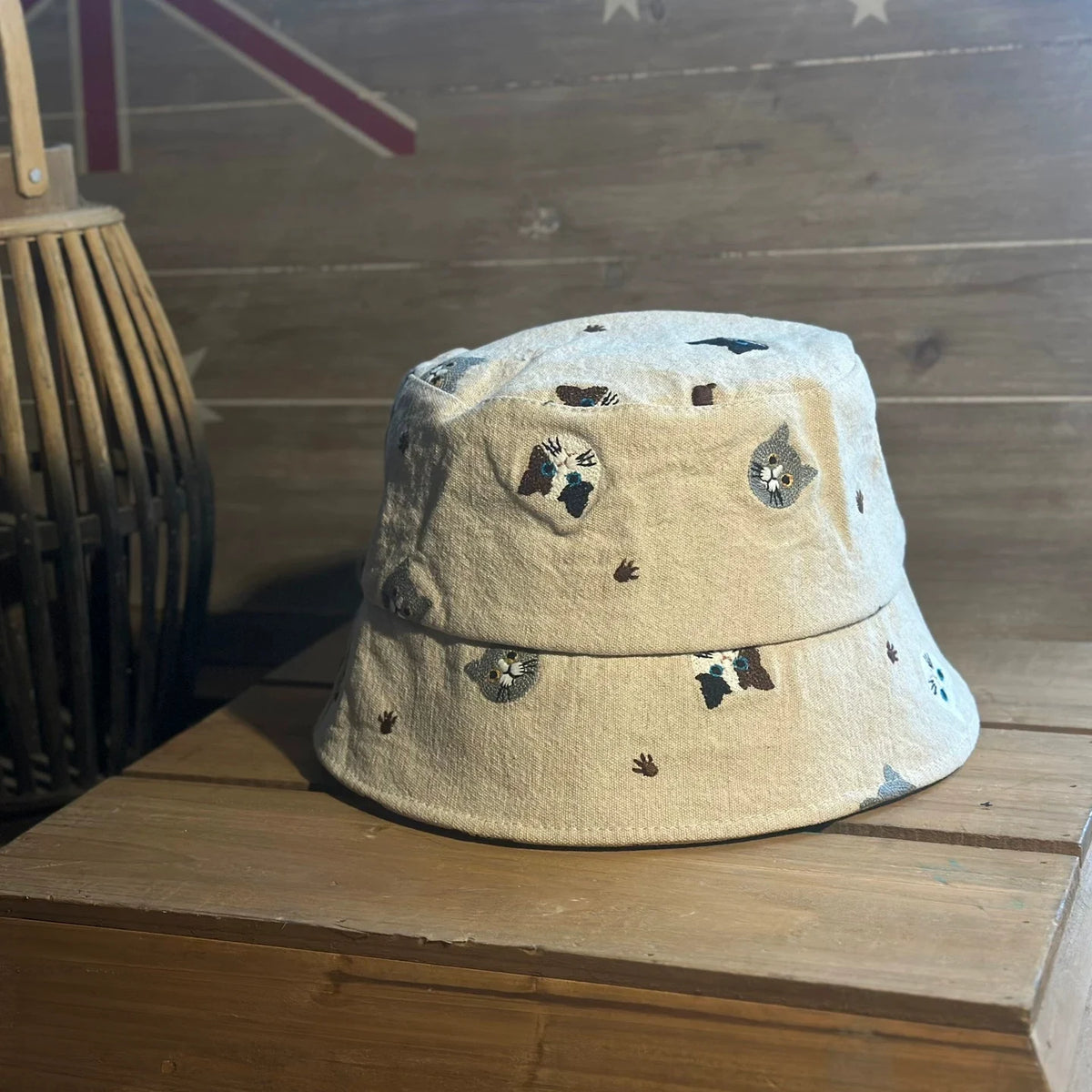 Beige embroidered cat cotton bucket hat shown from the front on a wooden table