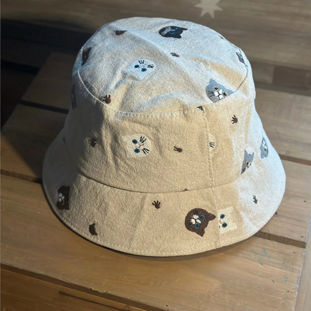Angled close-up of a beige cotton bucket hat with embroidered cat motifs