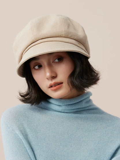 Front view of a beige newsboy cap showing its panelled crown and short curved brim on a model.