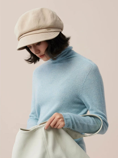 Model wearing a beige newsboy cap and light blue turtleneck while holding a pale green bag.