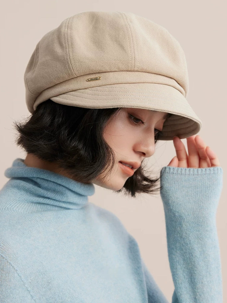 Side view of a beige newsboy cap showing its curved brim, rounded crown and small front badge.