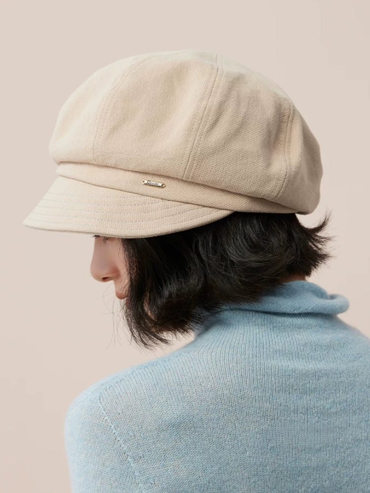 Model turned to the side in a beige newsboy cap, showing the hat's rounded crown above a short bob.
