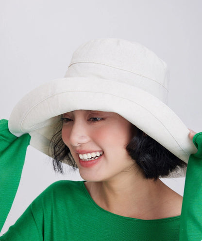 Smiling woman adjusting a beige packable wide brim sun hat with a relaxed floppy shape.