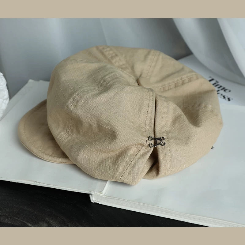 Beige slouchy cotton beret hat with elastic adjustable fit, styled on a book for a soft casual look