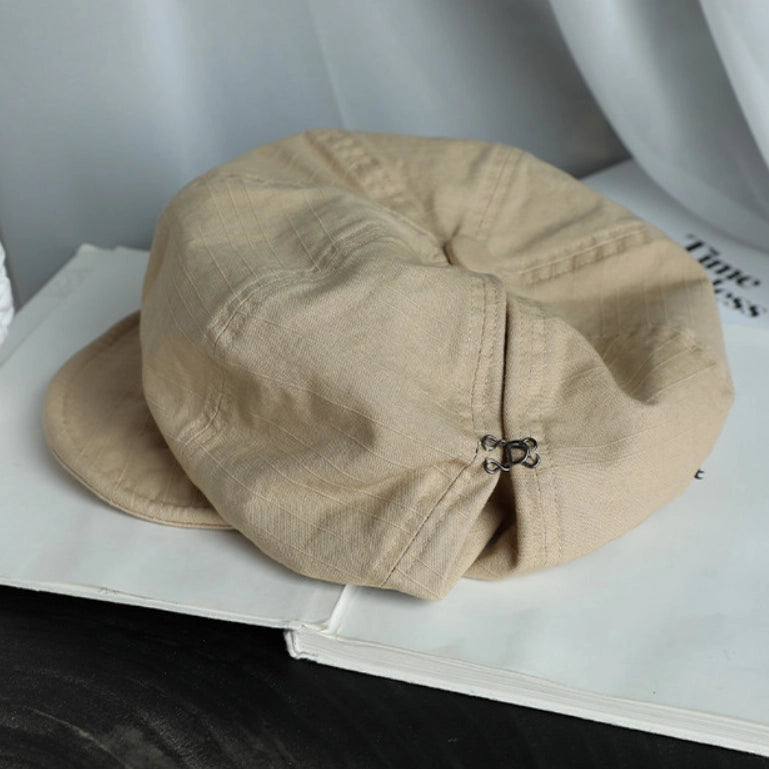 Beige cotton beret hat displayed on a book, featuring a breathable fabric and casual slouchy silhouette