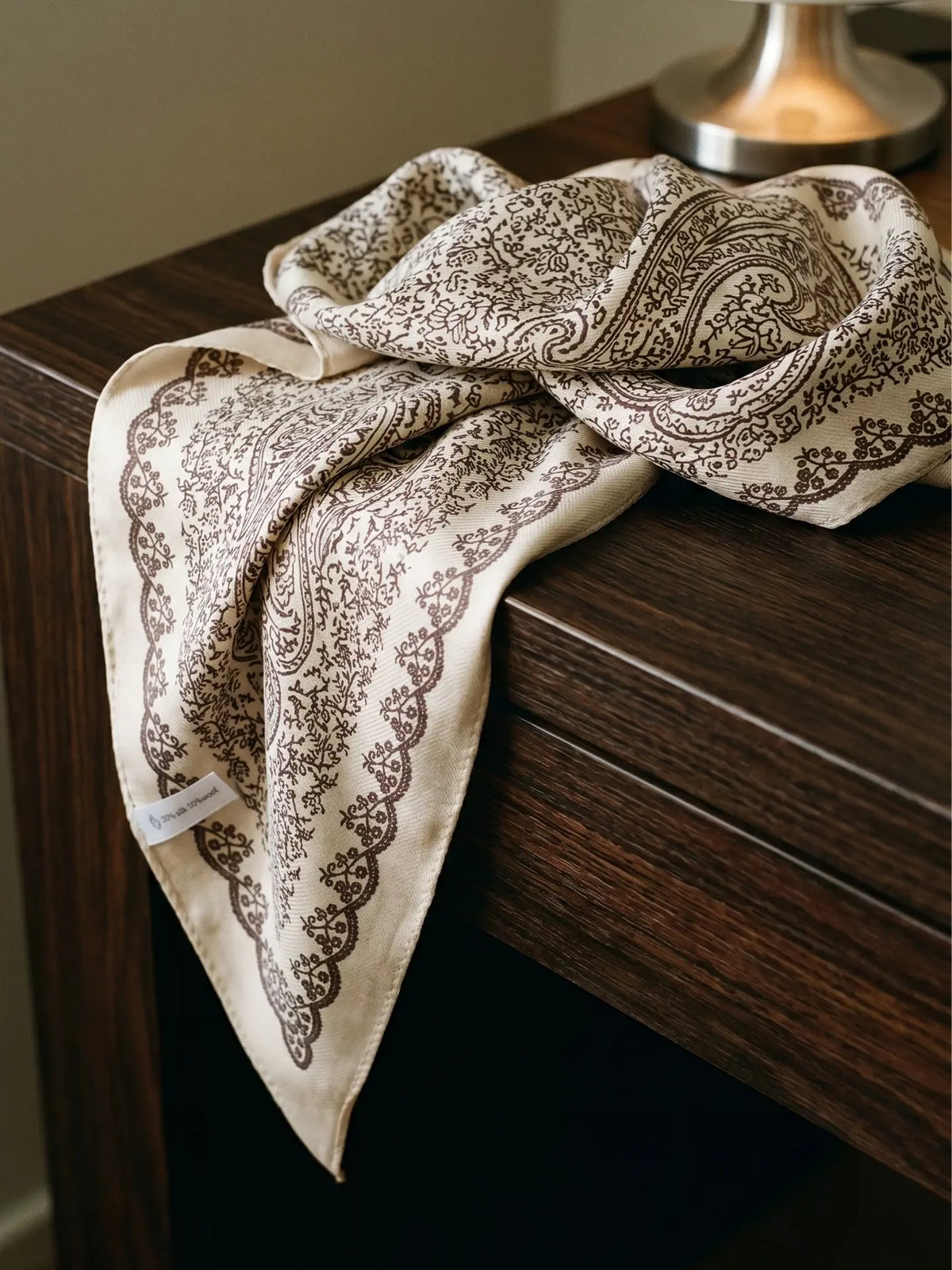 Beige floral silk wool scarf draped on a wooden table to show its soft texture and pointed ends