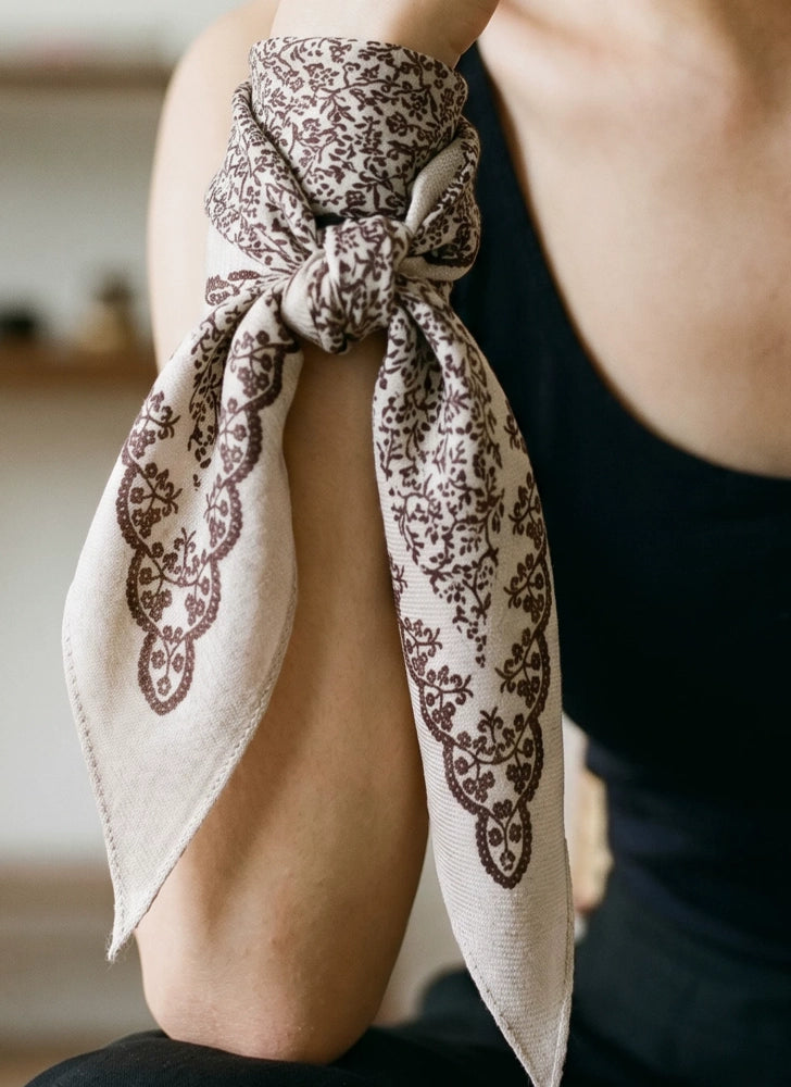 Close-up of a beige vine floral silk wool scarf tied in a soft neck knot