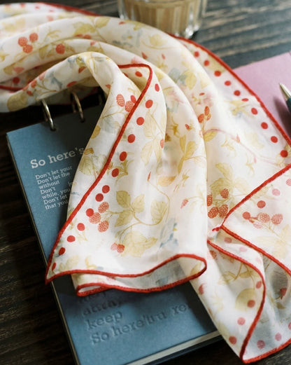 Ivory mulberry silk scarf with berry and rabbit print draped over books