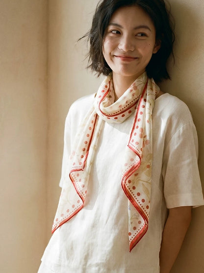 Woman wearing a berry print silk skinny scarf draped over a white blouse