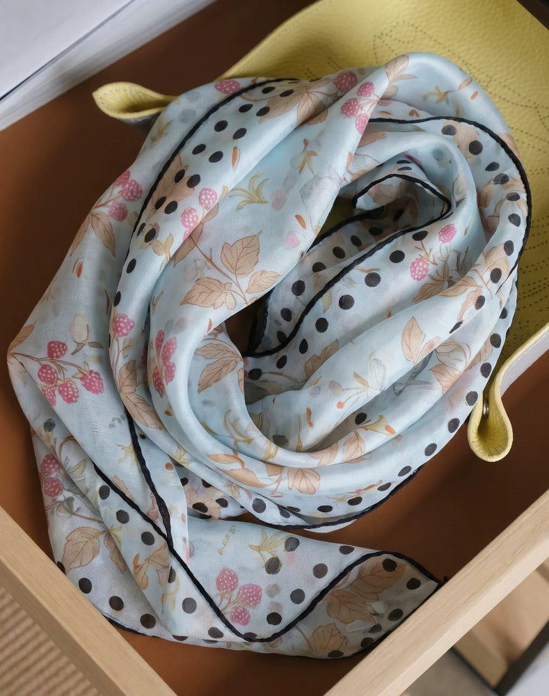 Sky blue botanical rabbit print silk skinny scarf coiled beside a yellow cushion