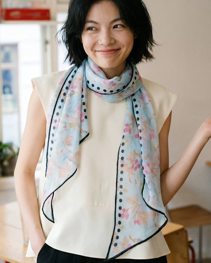 Woman wearing a sky blue berry and rabbit print silk scarf with long draped ends