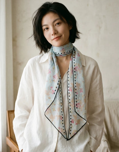 Woman styling a sky blue botanical silk skinny scarf with a white blouse