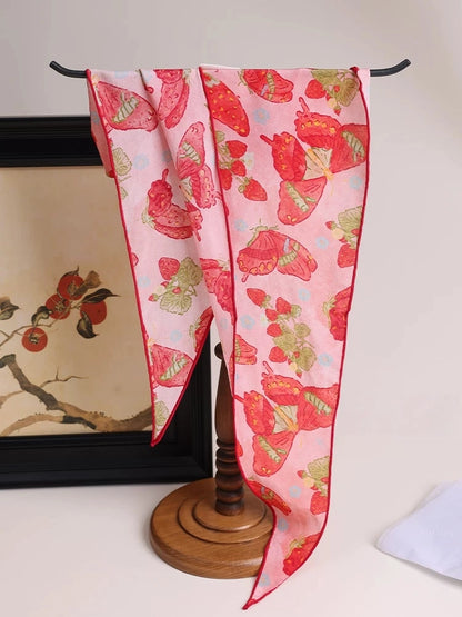 Berry red silk scarf with butterfly print draped near handbag, elegant accessory detail