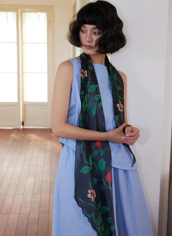 Long black botanical silk scarf styled over a sleeveless blue dress
