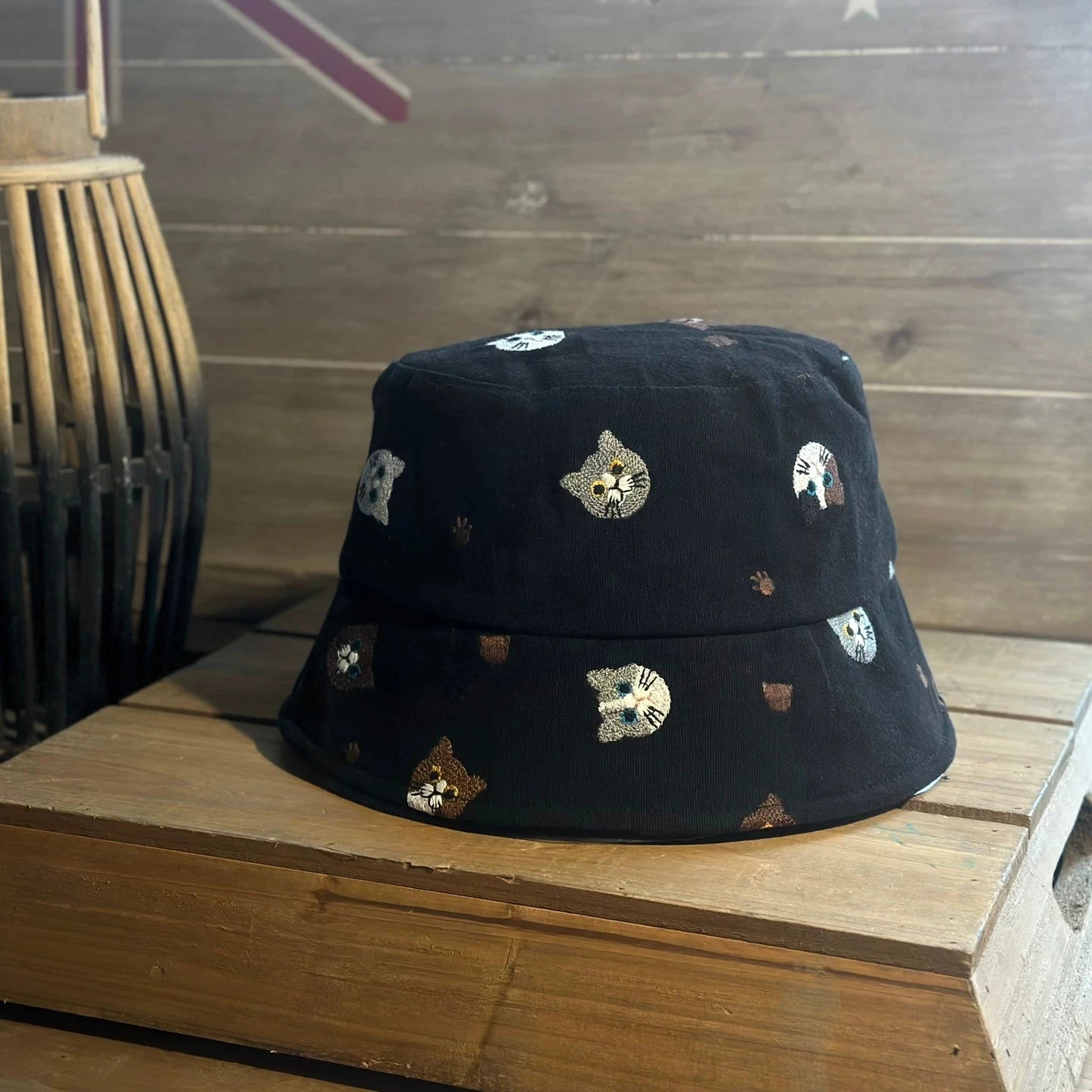 Black embroidered cat cotton bucket hat shown from the front on a wooden table