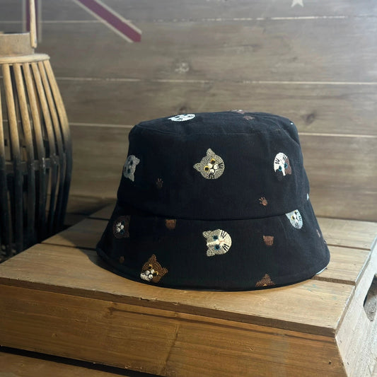 Black embroidered cat cotton bucket hat shown from the front on a wooden table