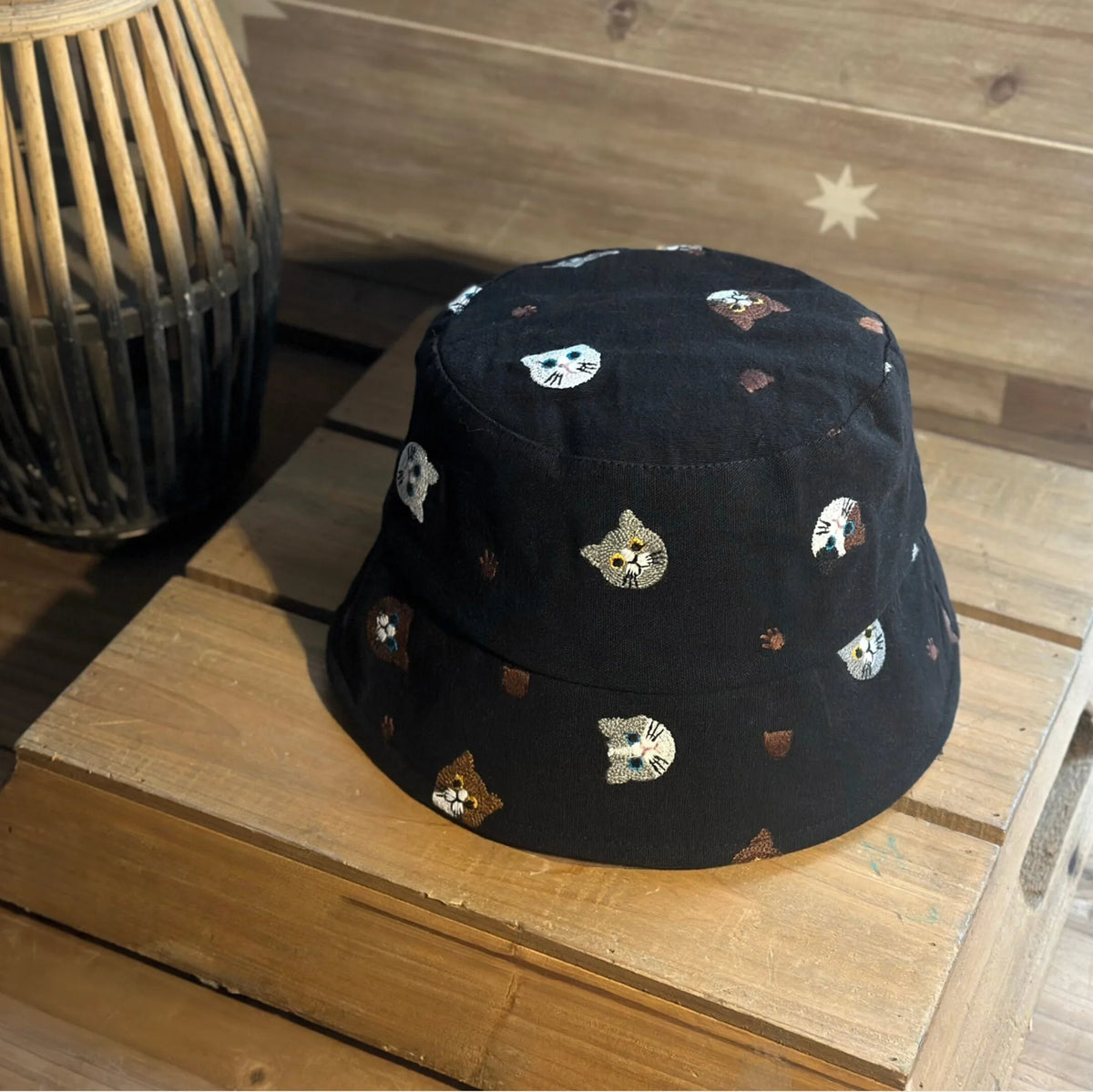 Angled view of a black cotton bucket hat with colorful embroidered cat faces