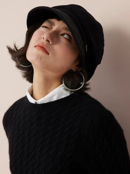 Model looking upward while wearing a black newsboy cap with a rounded crown and curved brim.