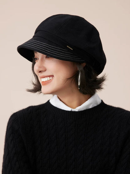 Side view of a black newsboy cap showing its rounded crown and rows of stitching along the brim.