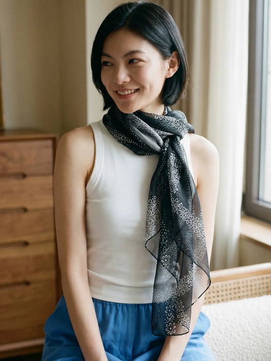 Woman styling a lightweight black floral silk chiffon scarf with a white sleeveless top