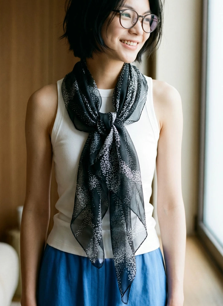 Woman wearing a long sheer black floral silk scarf in a relaxed draped neck style