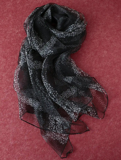 Sheer black floral mulberry silk chiffon scarf arranged on a textured red background