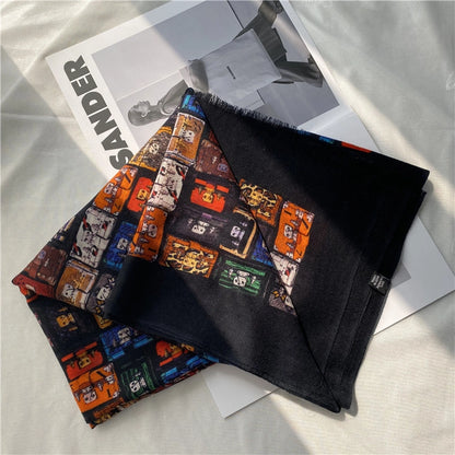 Folded black fine wool scarf with a multicolor trunk print and solid black reverse styled beside a magazine