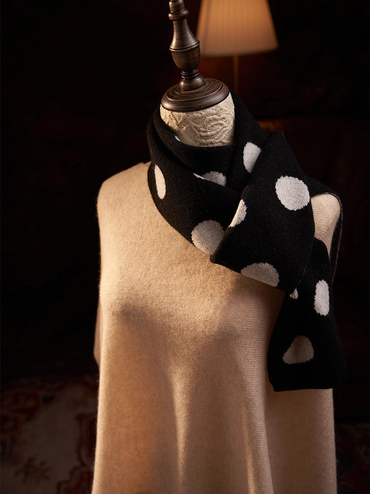 Black cashmere scarf with cream polka dots looped around the neck, with the ends falling to one side.