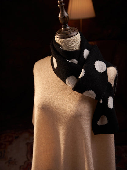 Black cashmere scarf with cream polka dots looped around the neck, with the ends falling to one side.