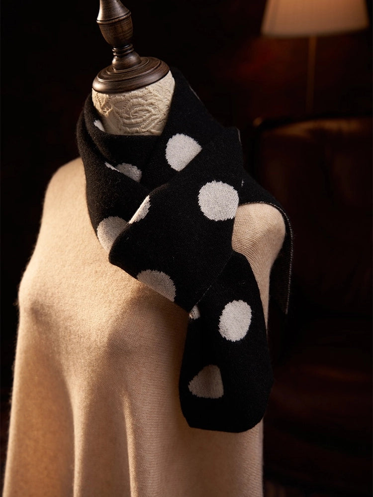 Close-up of a black polka dot cashmere scarf crossed at the neck over a camel sweater.