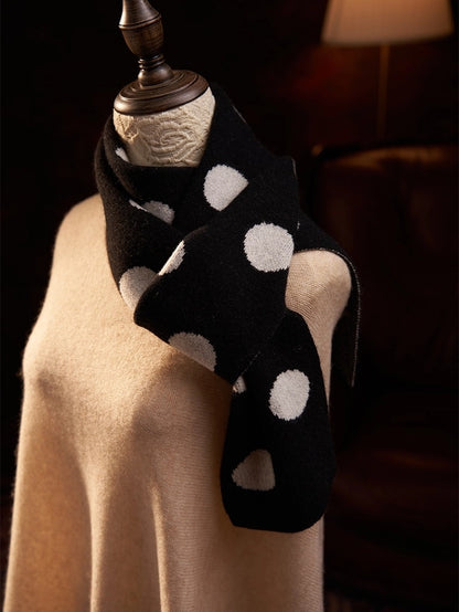 Close-up of a black polka dot cashmere scarf crossed at the neck over a camel sweater.