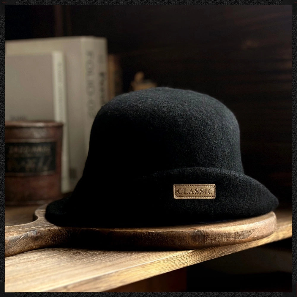 Front view of a black rolled brim wool felt cloche hat displayed on a wooden board