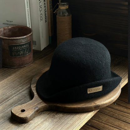 Black wool felt cloche hat with a dome crown and upturned brim in a vintage tabletop setting