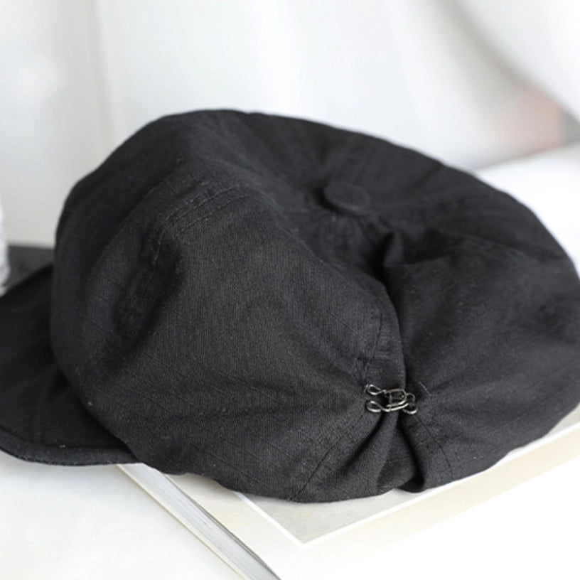 Black slouchy cotton beret displayed on a book, featuring soft cotton texture and minimalist casual style