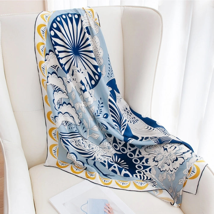 Blue bird and flower silk scarf draped on a chair, featuring a glossy large square scarf design.
