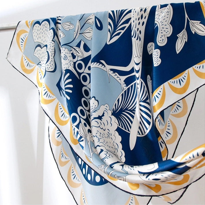 Close-up of soft luxury silk scarf with blue floral, bird, and abstract print details.