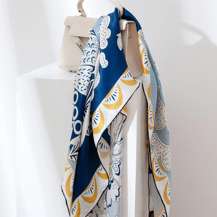 Large silk square scarf hanging with navy blue floral bird print and refined artistic border.