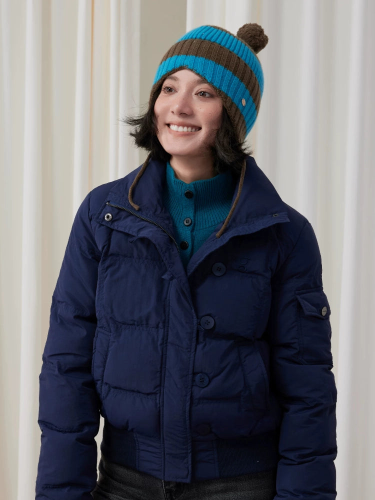 Model wearing a blue and brown striped wool earflap beanie with a navy puffer jacket.