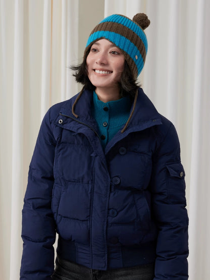 Model wearing a blue and brown striped wool earflap beanie with a navy puffer jacket.