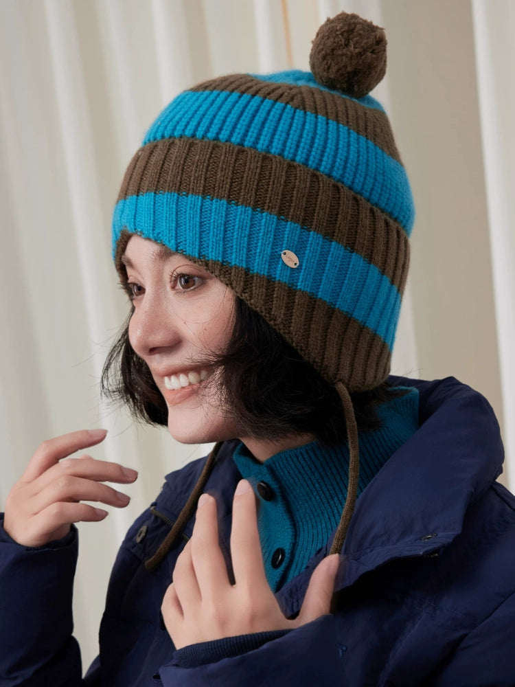 Three-quarter view of a blue and brown striped wool earflap beanie with a brown pom pom and hanging ties.