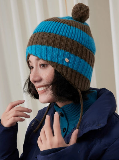 Three-quarter view of a blue and brown striped wool earflap beanie with a brown pom pom and hanging ties.