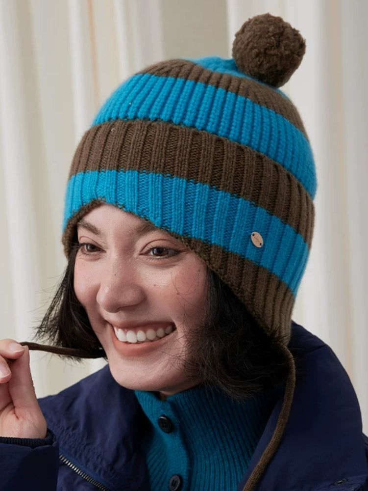 Smiling model wearing a blue and brown striped wool earflap beanie in a front close-up.
