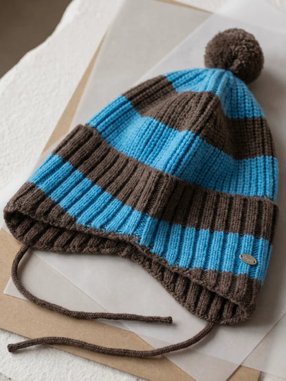 Blue and brown striped wool earflap beanie laid flat, showing ribbed knit, a brown pom pom and ties.