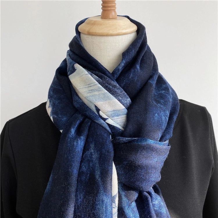 Close view of a lightweight blue wool scarf crossed at the neck with an ivory wave accent